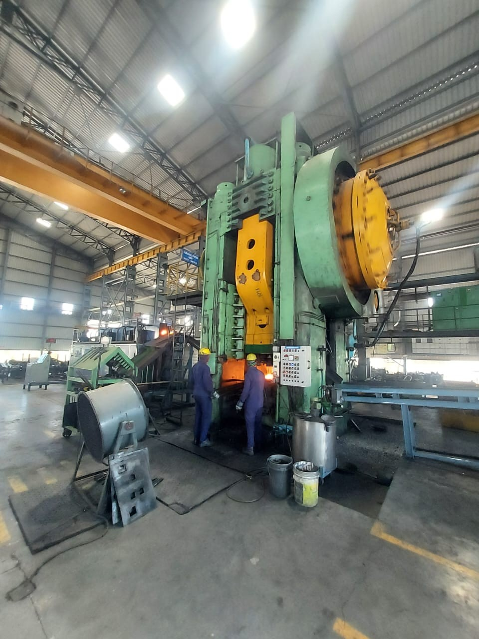 Our team on the forging press floor in India · two operators in branded uniforms inspecting the press