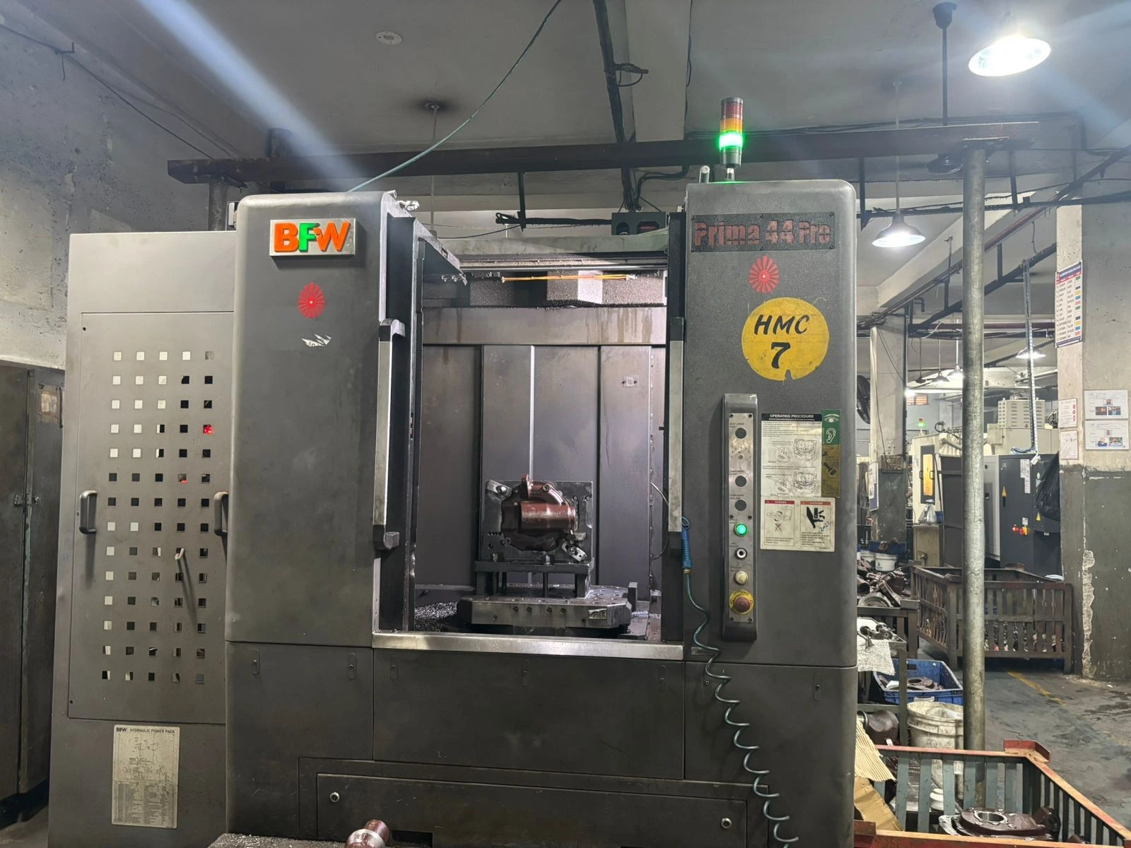 CNC machining bay at our Pune partner facility, India · multi-axis centers, control panels, operator in PPE during a production run