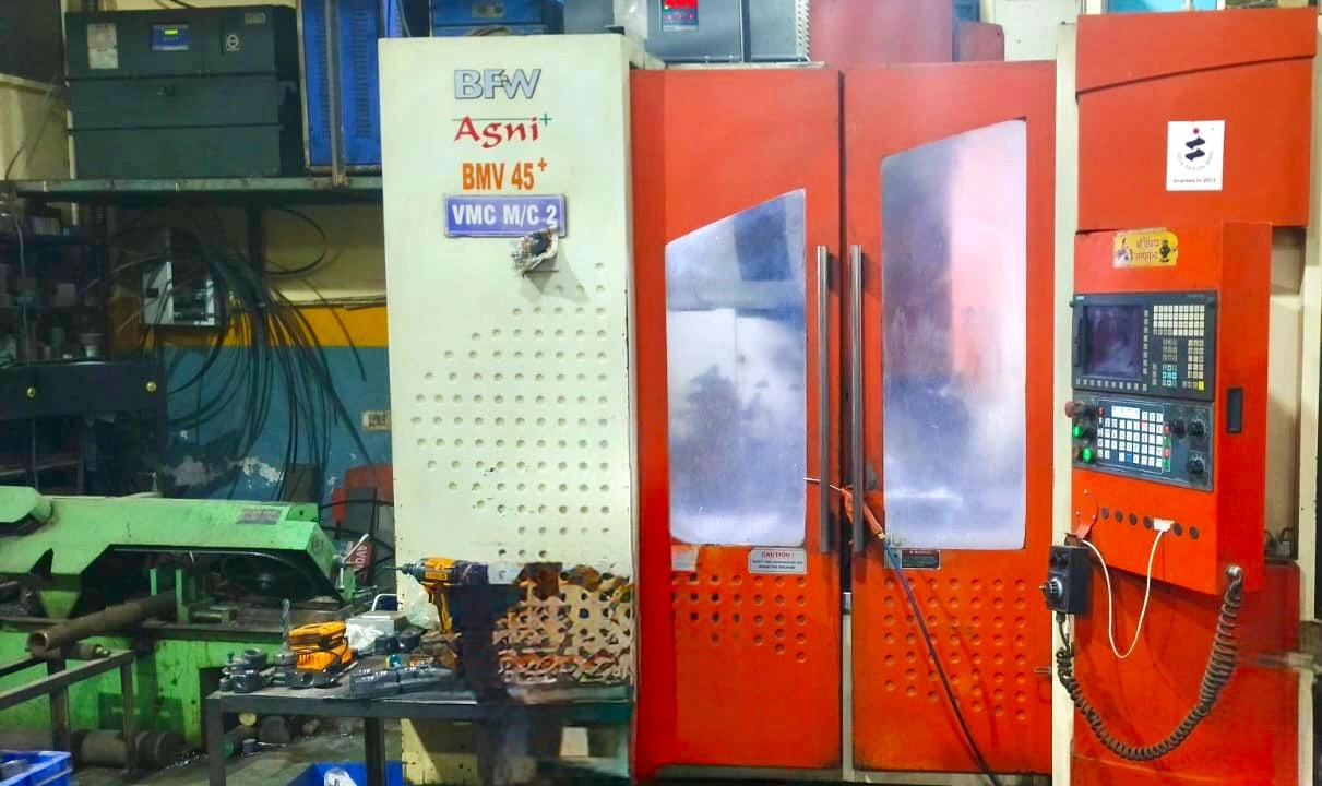 Cylindrical grinding wheel finishing a hardened steel shaft to micron tolerance at a VIA INDIGOS partner facility in India, sparks visible