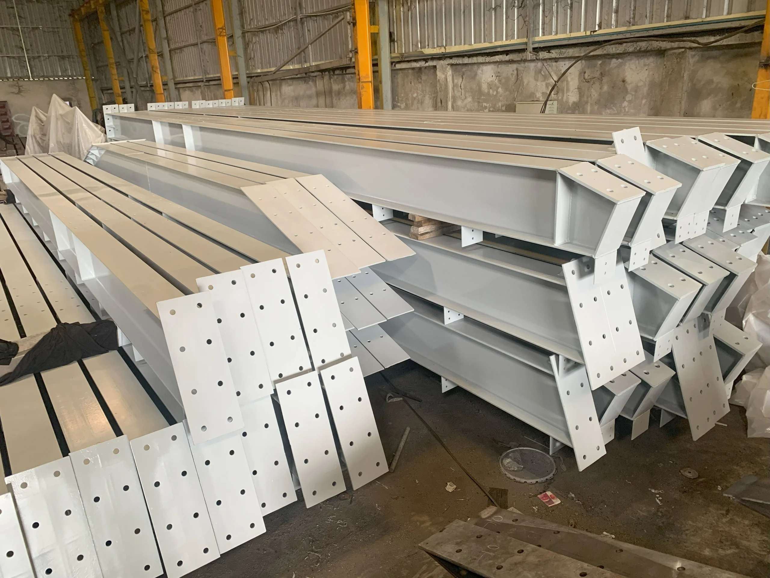 Fabricated structural steel beams built up from welded flange and web plates with bolt hole endplates on the floor at our India partner facility