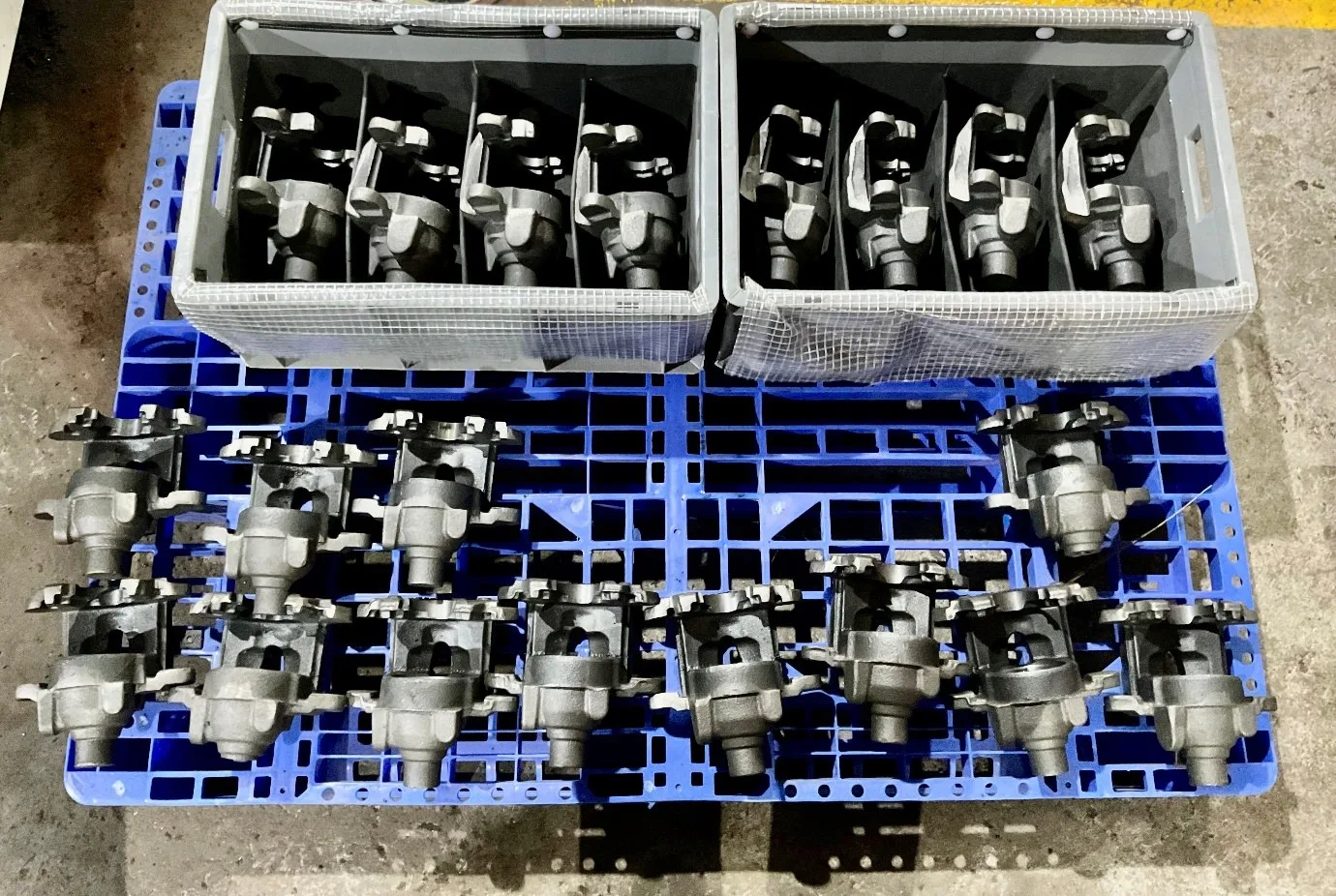 Cast iron brake caliper castings arranged in plastic crates and on a blue pallet at a VIA INDIGOS partner facility in India, post shot blast and ready for kitting and dispatch