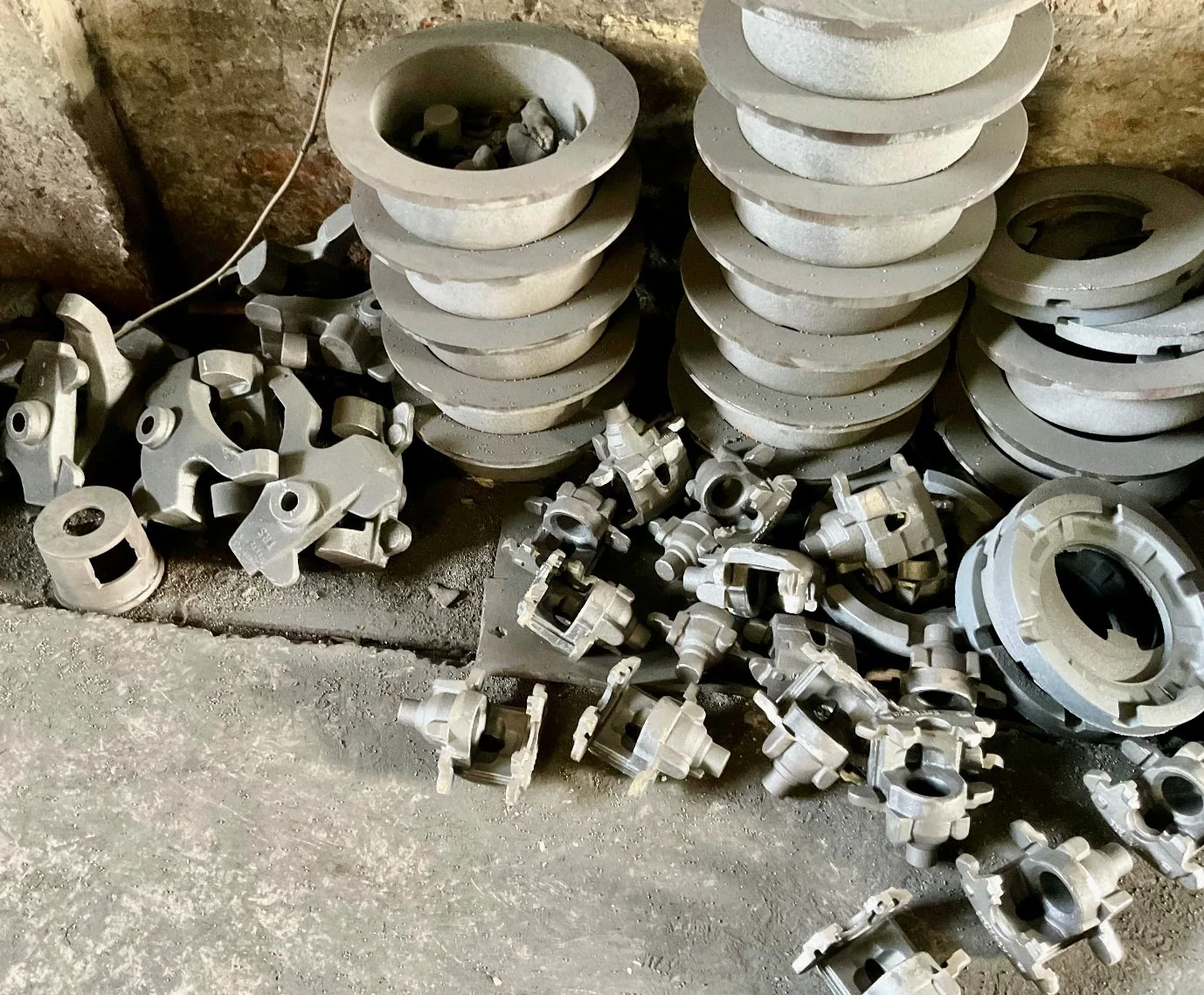 Variety of as-cast iron parts including rocker arms, pot castings, and gear hubs on the floor of a VIA INDIGOS partner foundry in India, pre-fettling and pre-machining