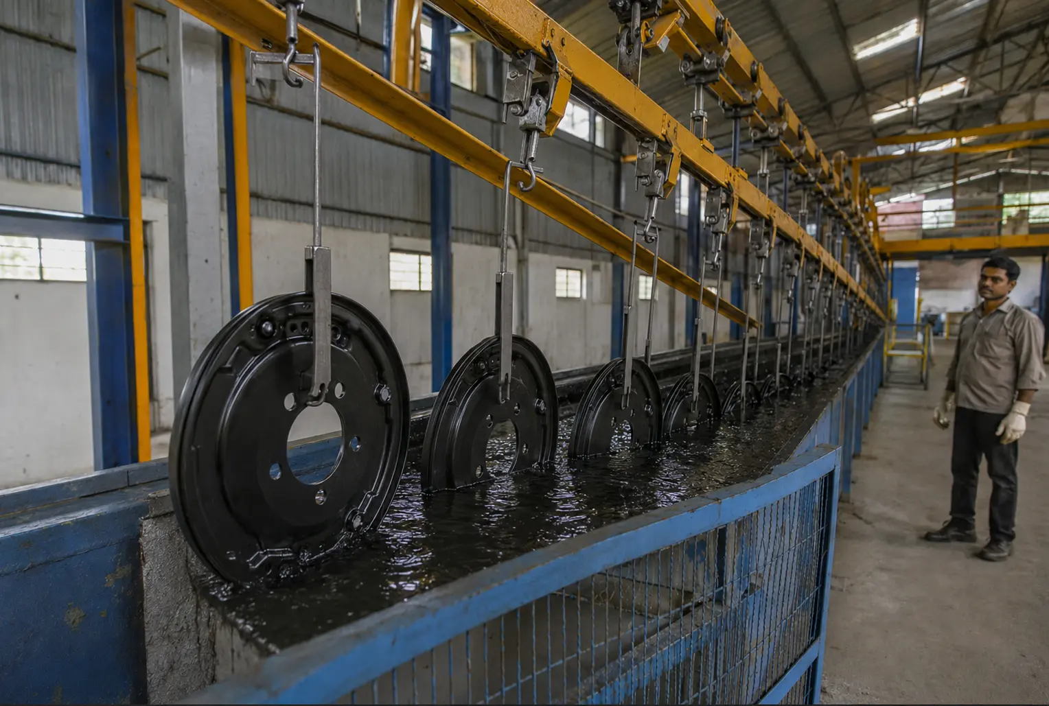 Brake backing plates entering a cathodic e-coat dip tank for full coverage coating in India